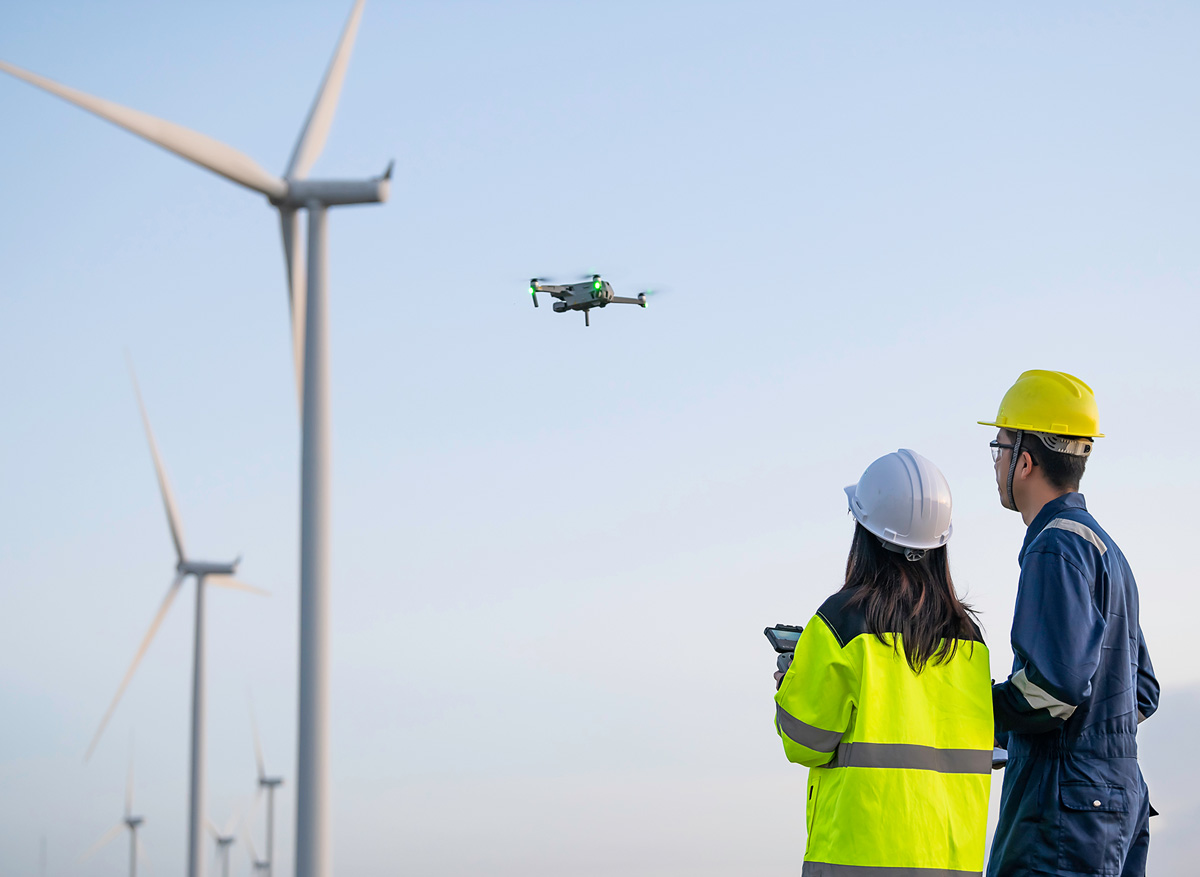 Twee ingenieurs staan in veld met windmolens terwijl ze een drone besturing