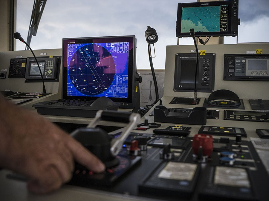 Hand operates steering of a ship, in background dashboard of a ship with satellite GPS system in view