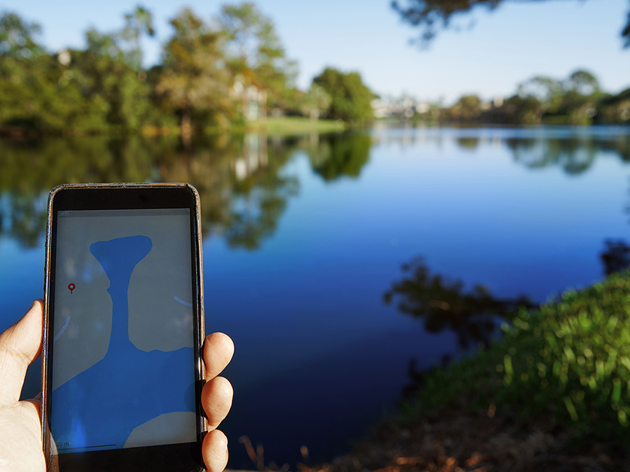 Main tenant un smartphone montrant une carte numérique avec un lac en arrière-plan